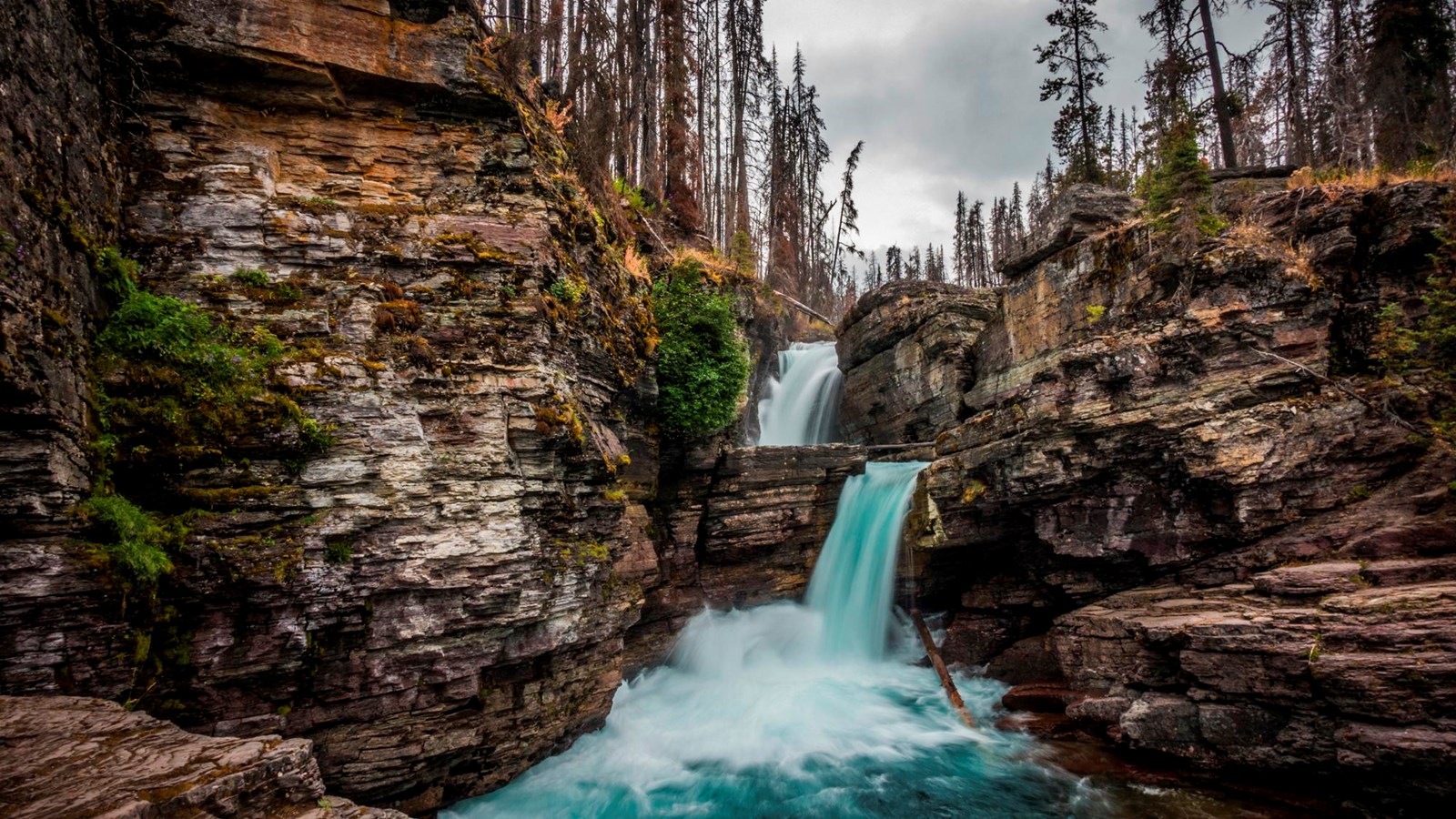 A double waterfall surrounded by cliffs with burned trees above.