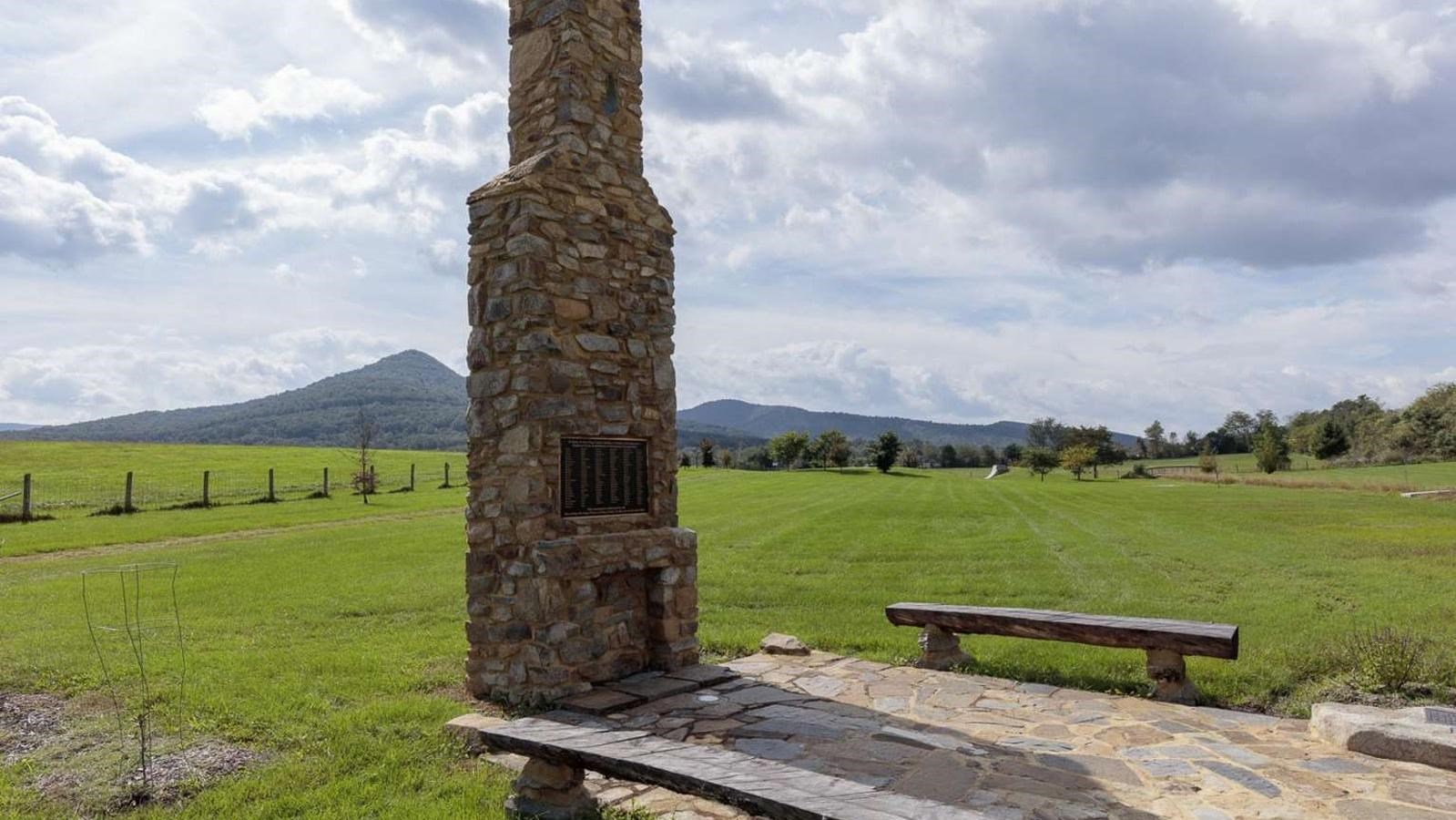 A tall stone chimney with a bronze plaque above the stone mantle; benches made of half logs flank.