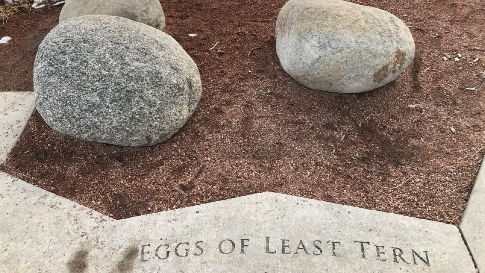 Three large, granite boulders sit arranged atop pea gravel. 