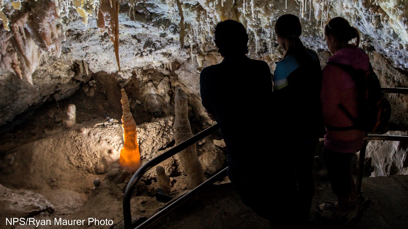 Three people looking over a railing at glowing cave formations