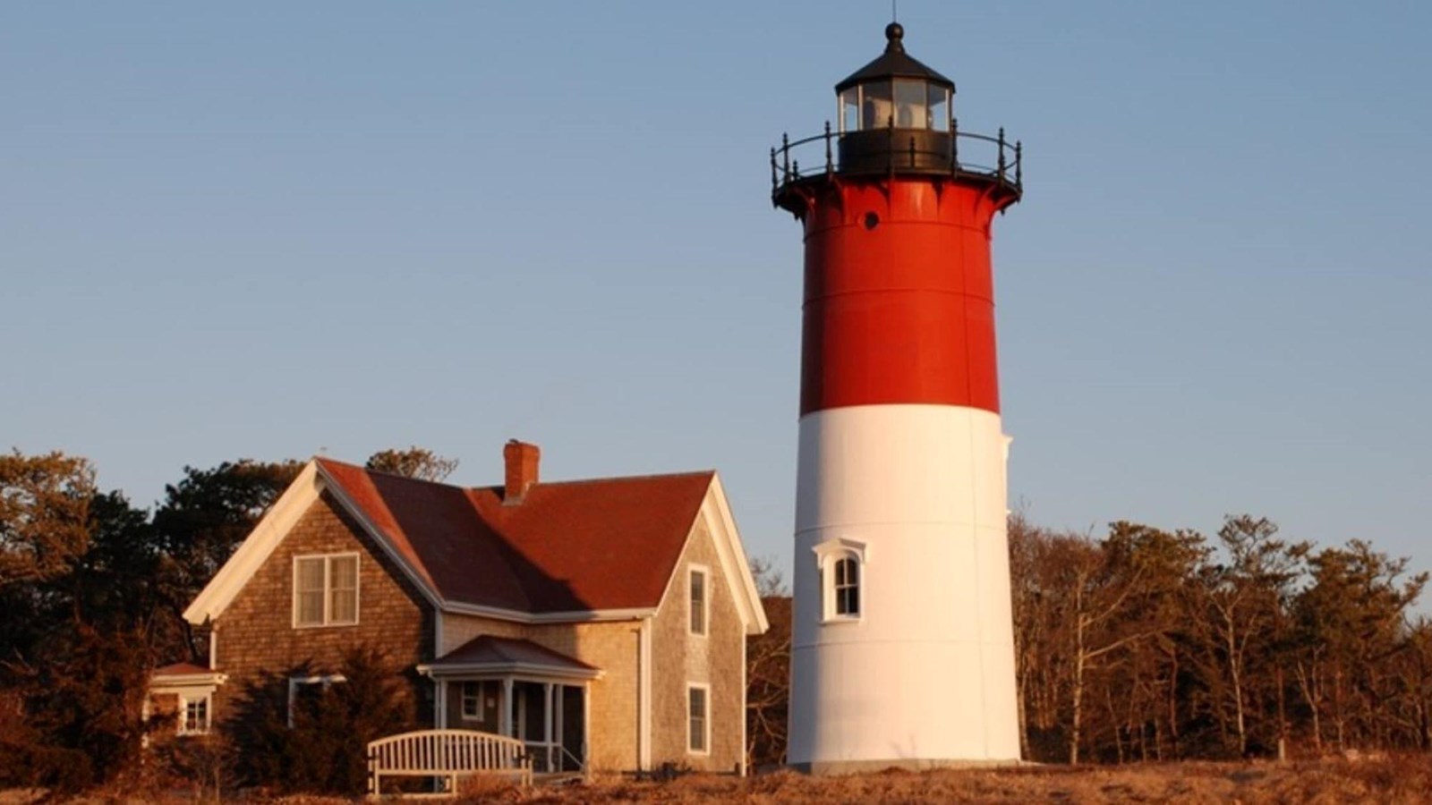 Nauset Light stands half white, half red, with the black light on top. A house stands adjacent.