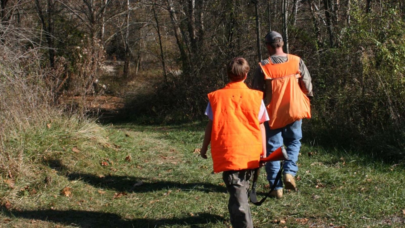 Two men walking in the woods wearing blaze orange hunting vests.