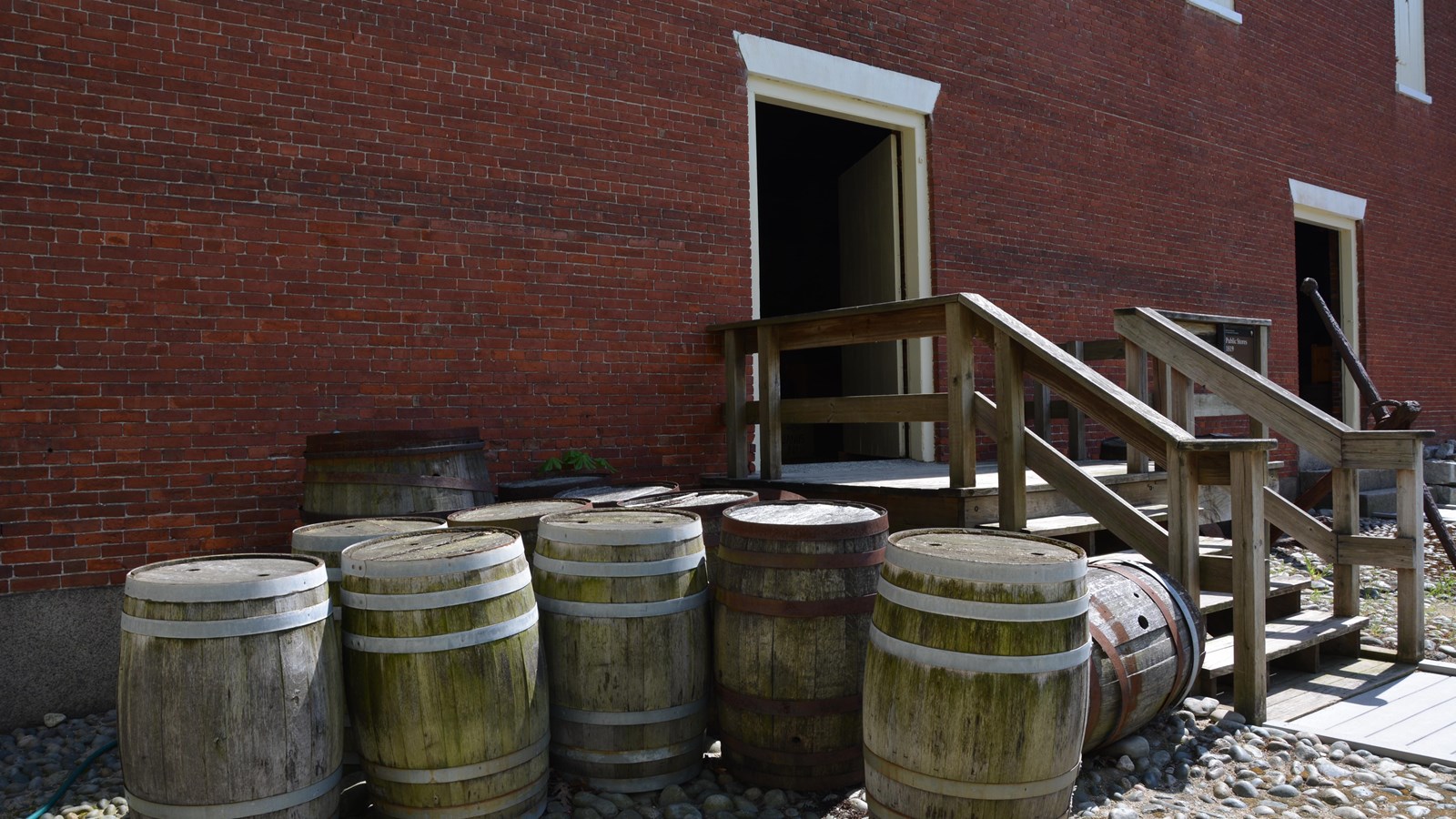 Brick building with wooden steps leading to entrance that is surrounded by barrels