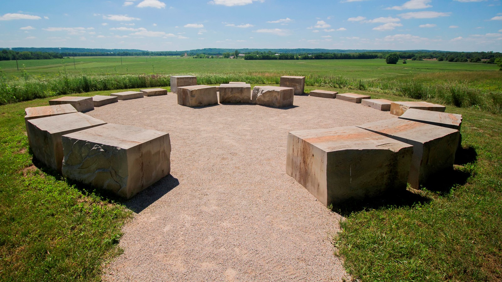 Large square stones patterned in a semi-circle placed upon gravel with grassy field in background