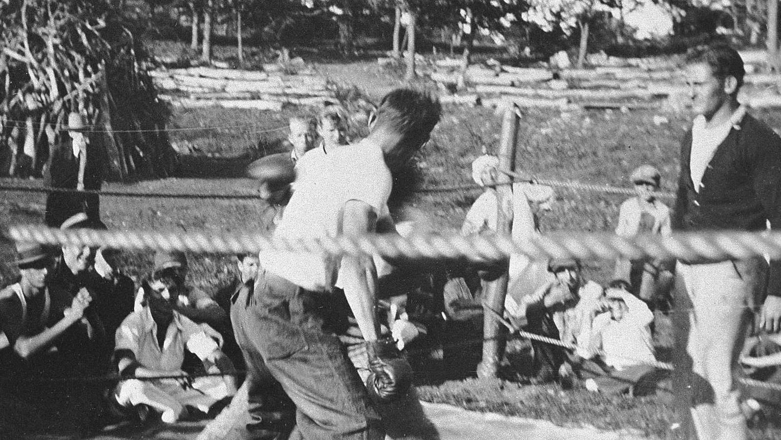 A man throws a punch during a boxing match in an outdoor ring at a CCC camp.
