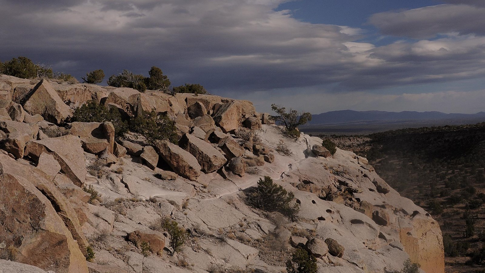 a carved trail across a tan cliff with cloudy skies behind
