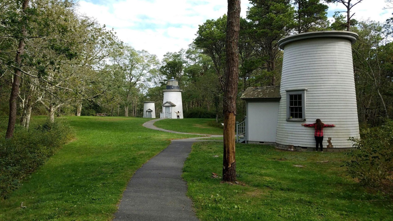 Three black and white lighthouses sit in a row in an open grassy space. A trail winds through them.