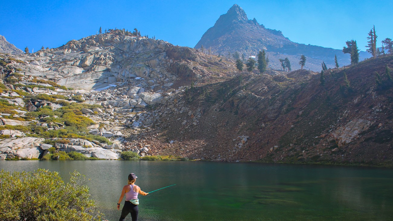 A woman fishing in an alpine lake surrounded by granite walls.