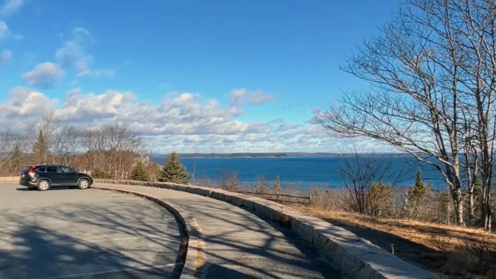 Two vehicles parked on an asphalt parking lot with a long, curved sidewalk and stone wall 