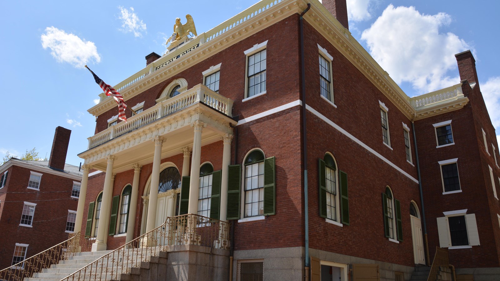 Three-story brick building with stone steps leading to entrance with columns and eagle on roof