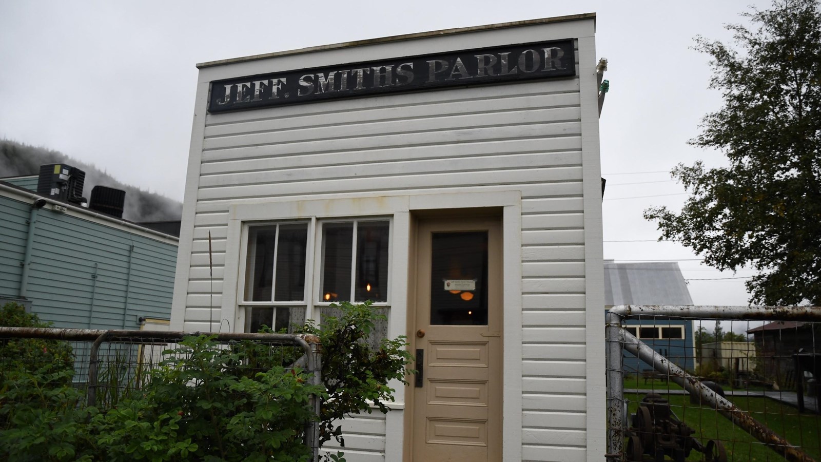 Narrow white building with tan door and black sign that reads 