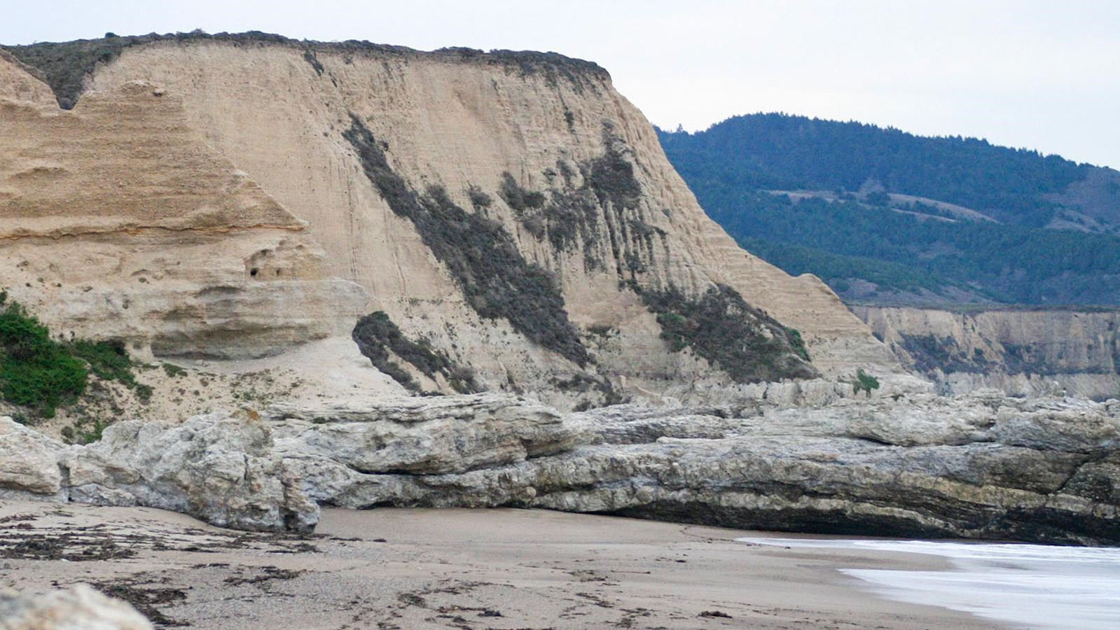 On the left, eroded bluffs rise above rock outcrops that stretch into a bay on the right.