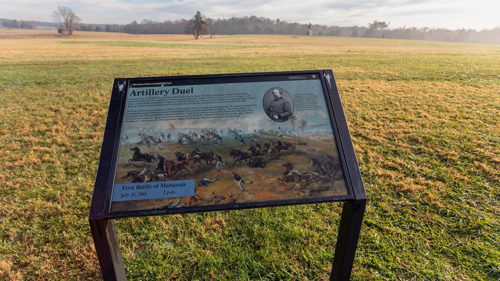 An informational panel in front of a grassy field. 