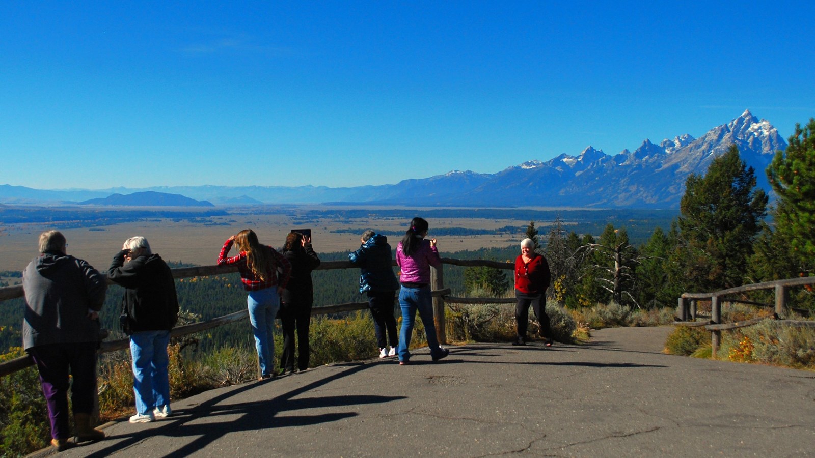 A group of seven people enjoy the views and take pictures of the valley and mountains.