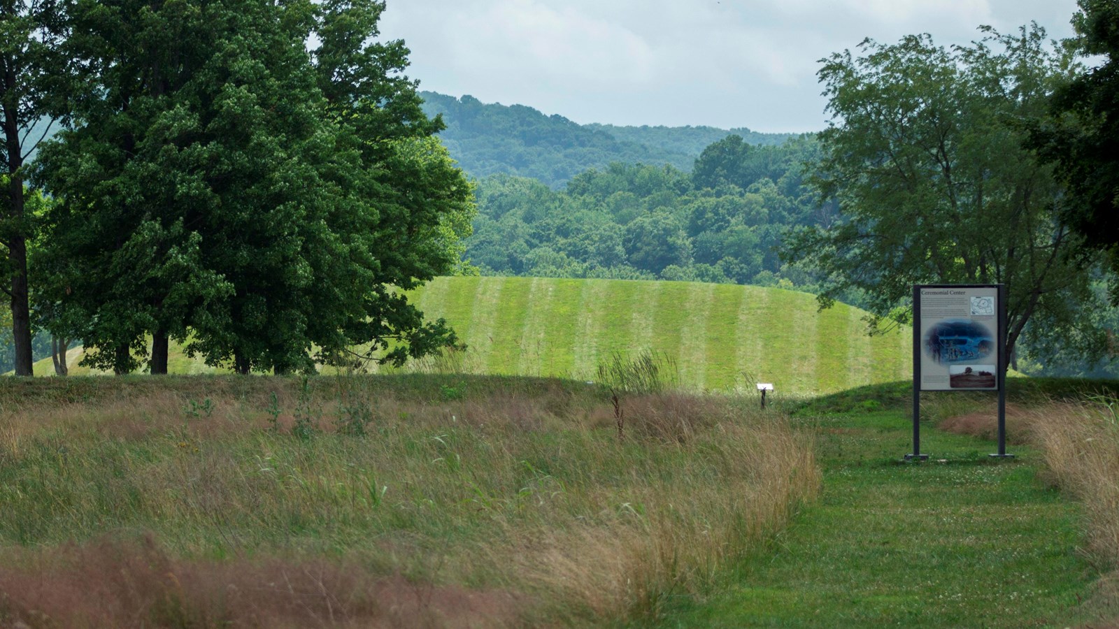 A mowed grass trail leads to a large grass-covered mound with back-and-forth mowed grass patterns