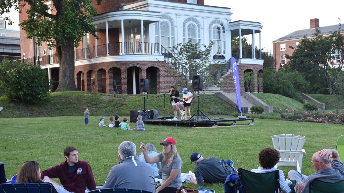 People sitting on a lawn enjoying a music concert.
