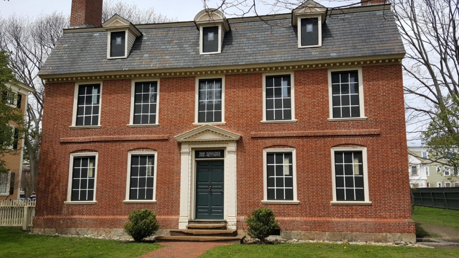 Three-story brick home with brick walkway leading to a green front door