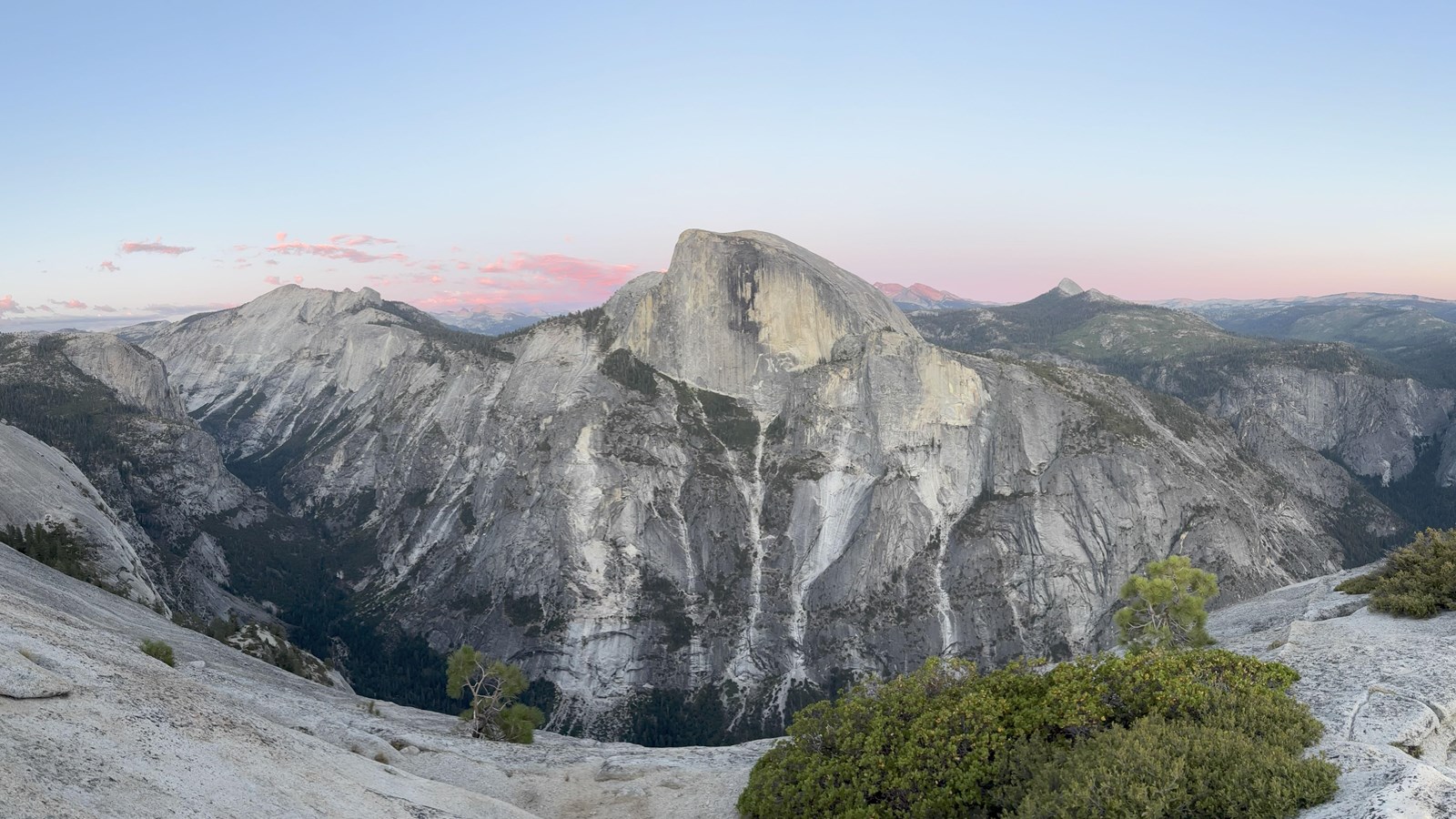 Panorama of Half Dome and granite gorges below pink sunset skies