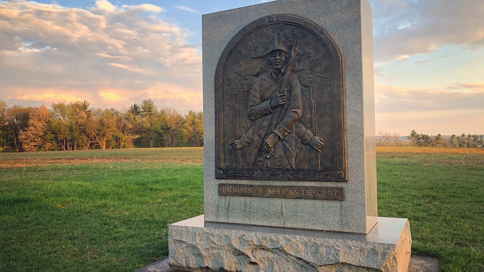 photograph, outdoors, grass, trees, stone monument, bas-relief bronze sculpture of three soldiers