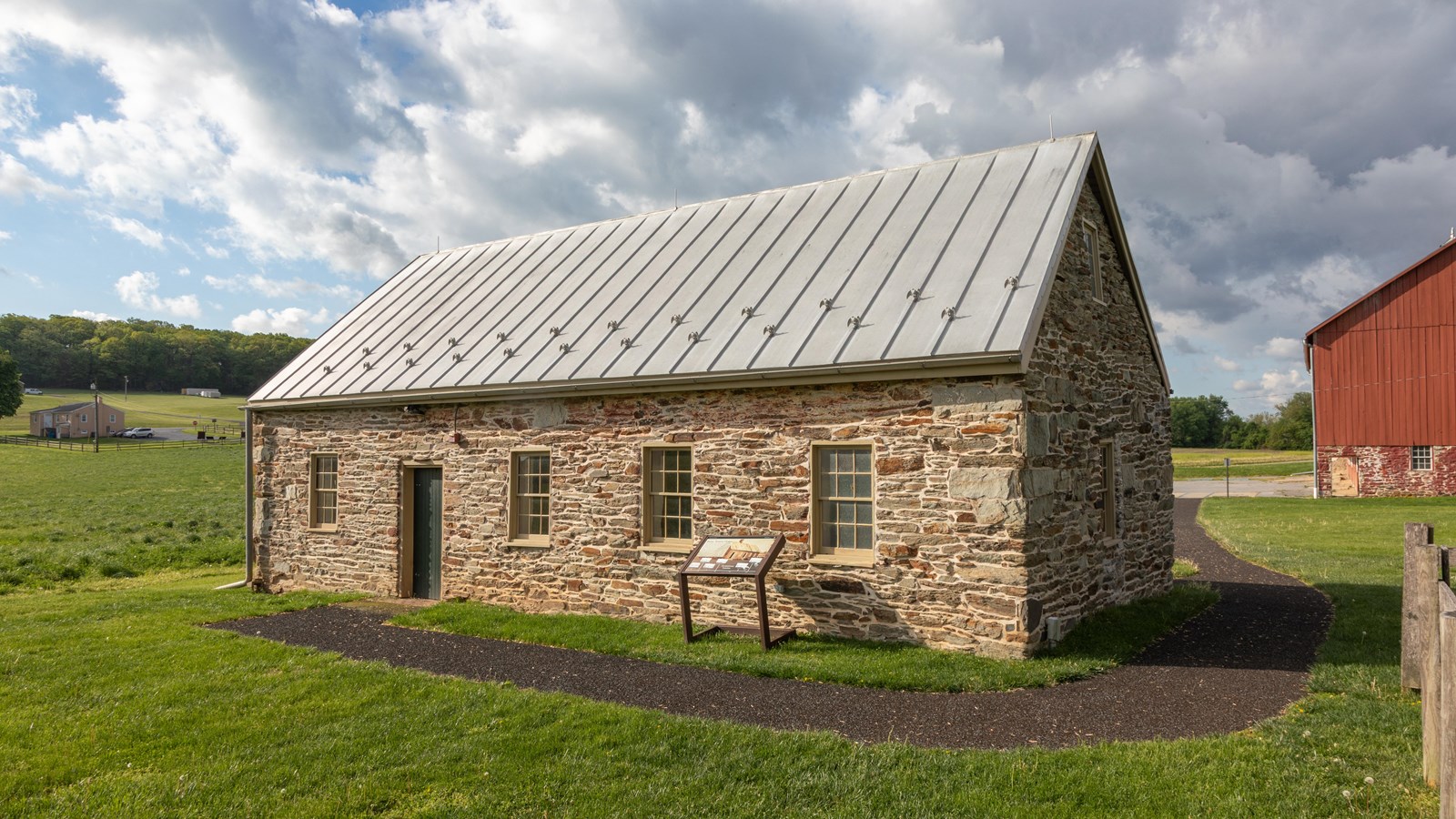 A one-story rectangular stone building surrounded by grass with a sidewalk leading to an open door.