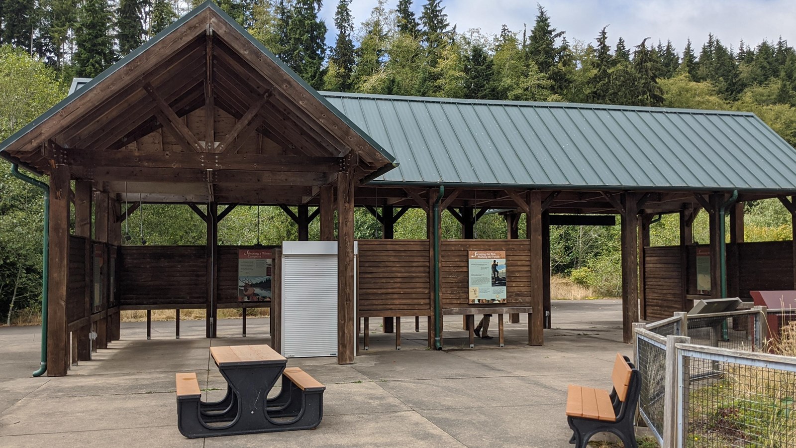 An L shaped open air plank picnic shelter, interpretive signs both inside and outside.