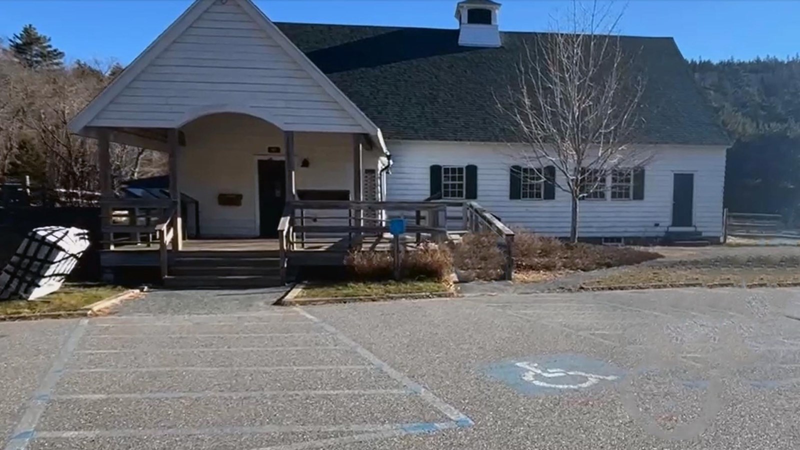 Asphalt parking lot with faded paint markings in front of a white building with a wheelchair ramp