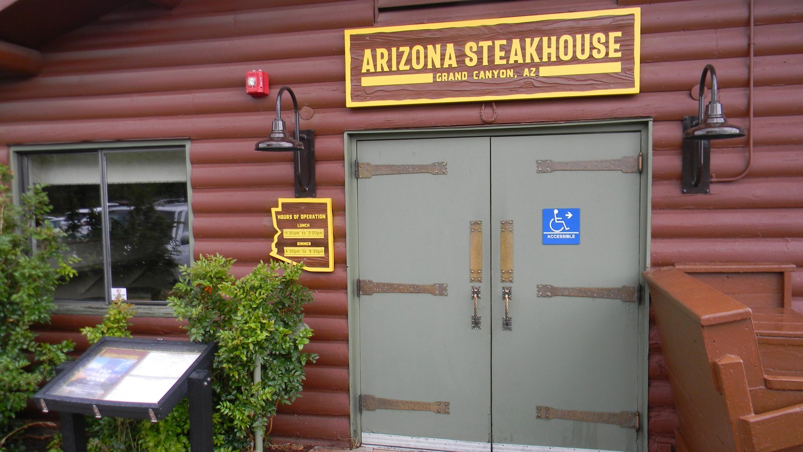 A large sign above a pair of metal double doors set in a wooden log wall reads 