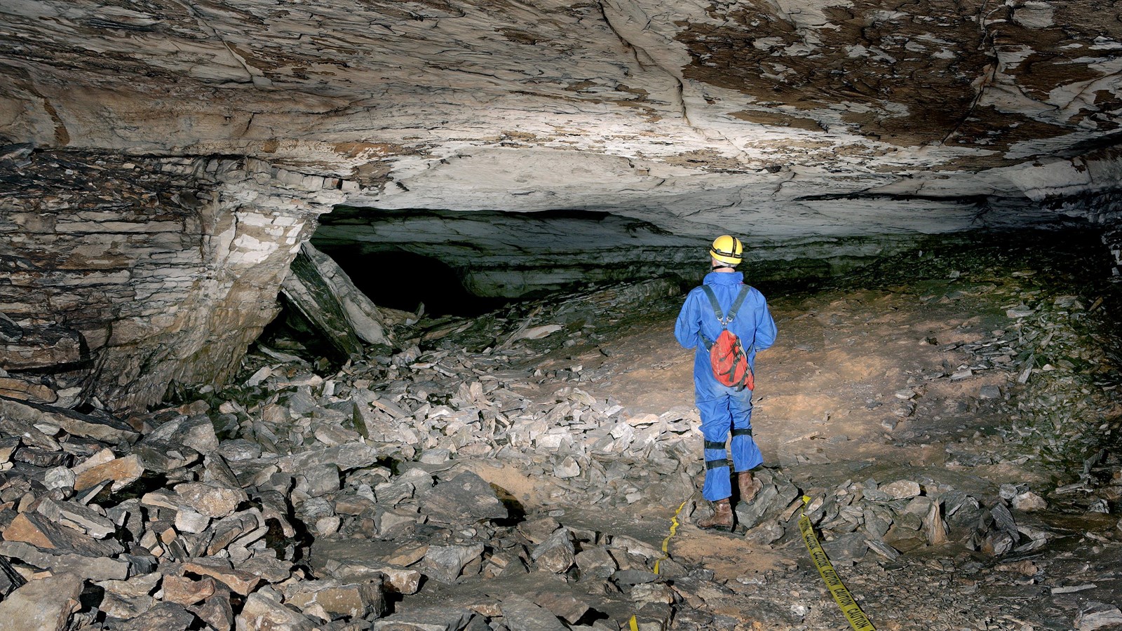 A cave scientist standing in a cave passage with crumbled rock all around them.