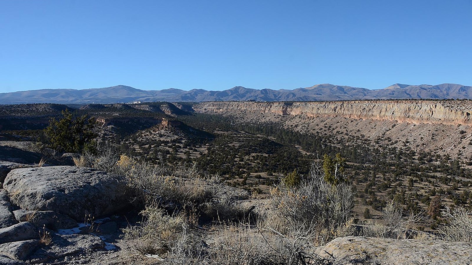 A distant view of a town with buildings on a distant mesa with mountain behind and a clear blue sky