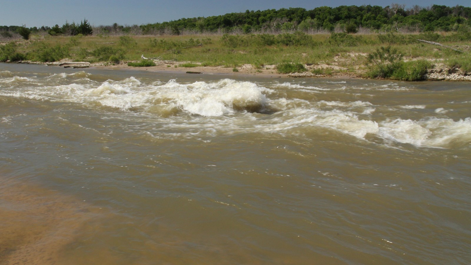 Rocks and ledges create rapids and turbulence in a riverbed and large white waves flow.