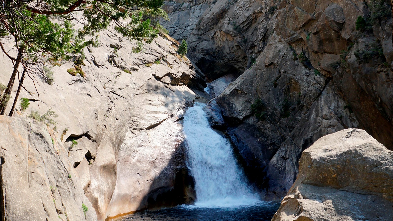 A powerful chute of water flows into a dark blue pool. Surrounded by high rock walls