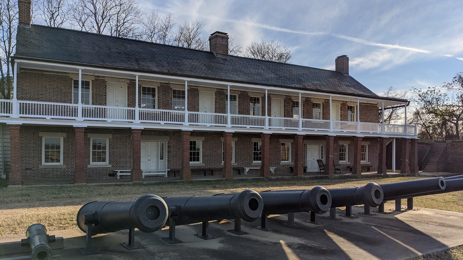 Large black cannons in front of a brick building with a wrap around porch and many white columns