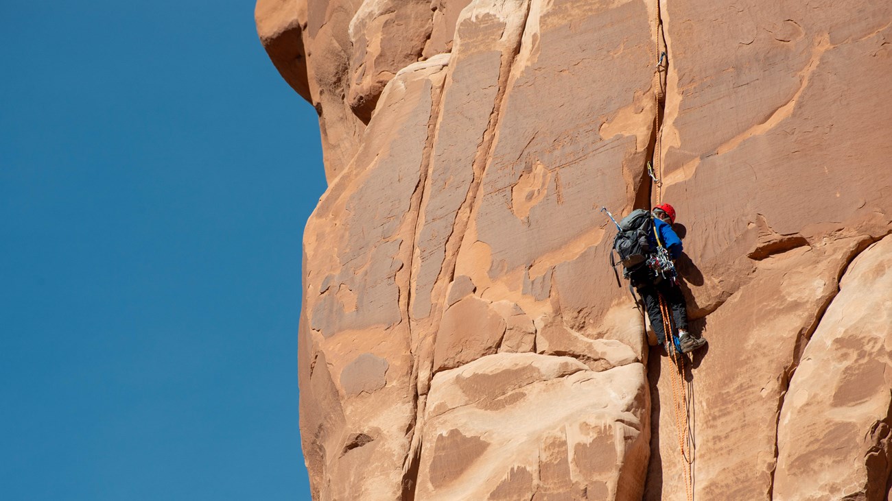 rock climber on vertical tan sandstone face, blue sky in background