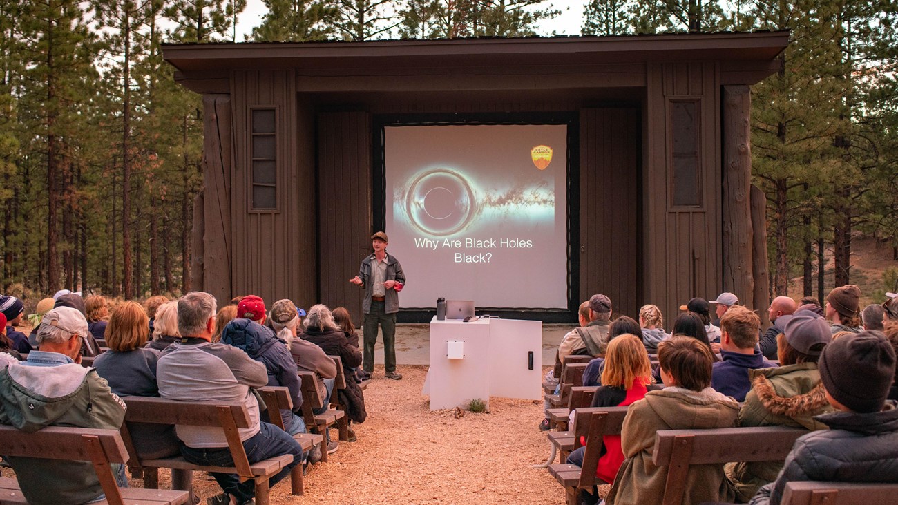 A ranger stands in front of a screen before a seated audience.