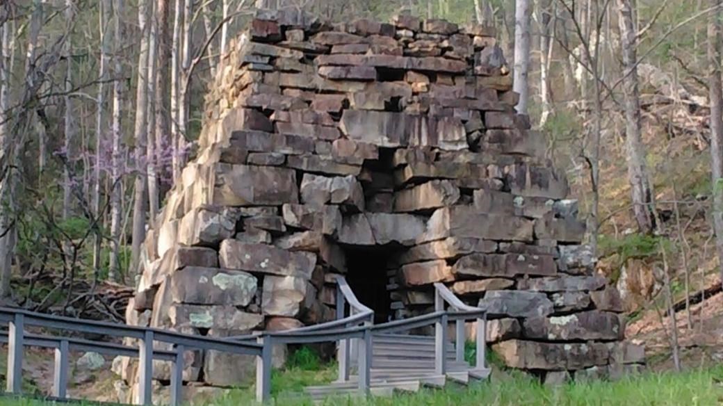 a stone structure shaped like a pyramid surrounded by grass, trees, and a wooden fence. 
