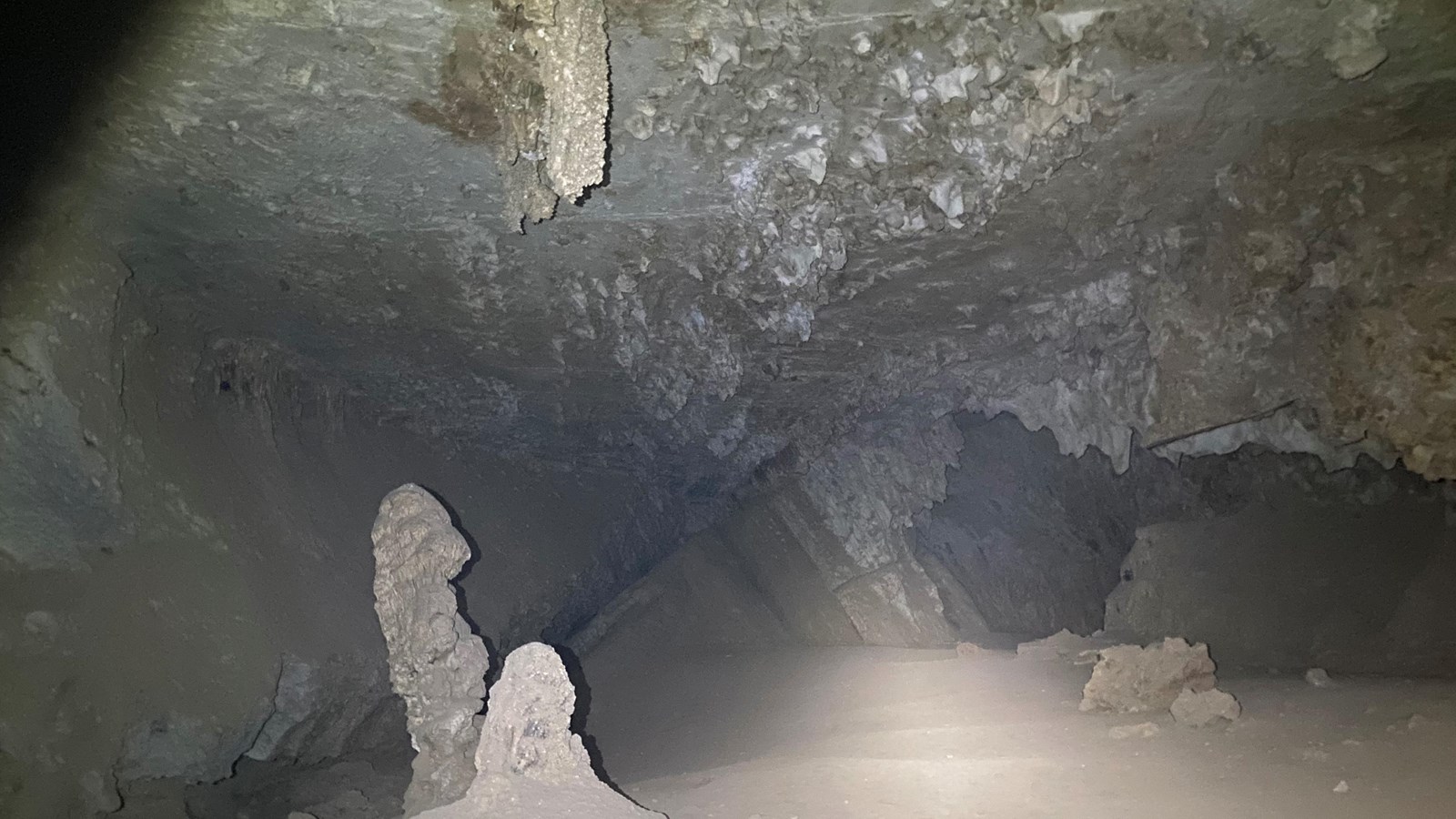 Interior view of cave with stalagmites in the foreground and stalactites hanging from the ceiling.