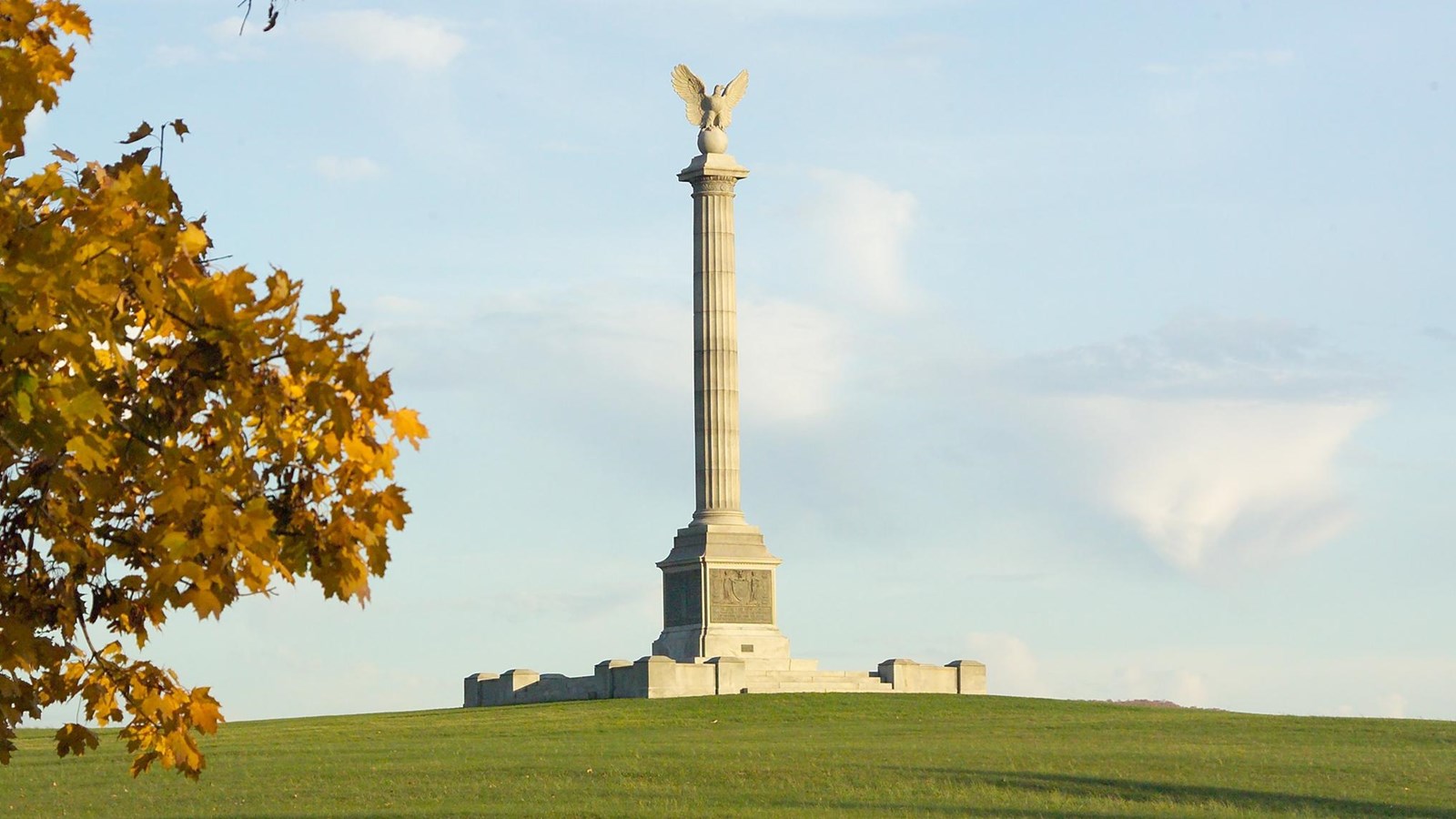 A tall stone column with a bird statue at the top sits on a ball. Bronze tablets are at the bottom.
