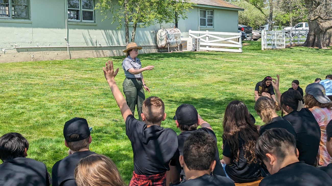 A ranger stands in front of a group of students, while one raises his hand.