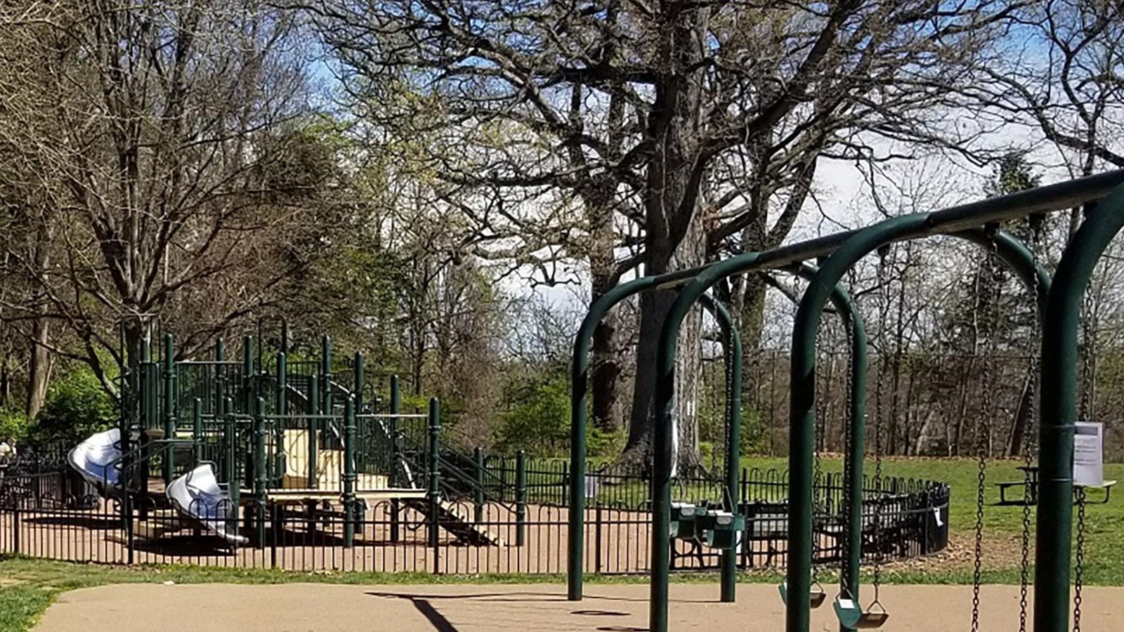 Slides enclosed by a wood fence behind a set of swings