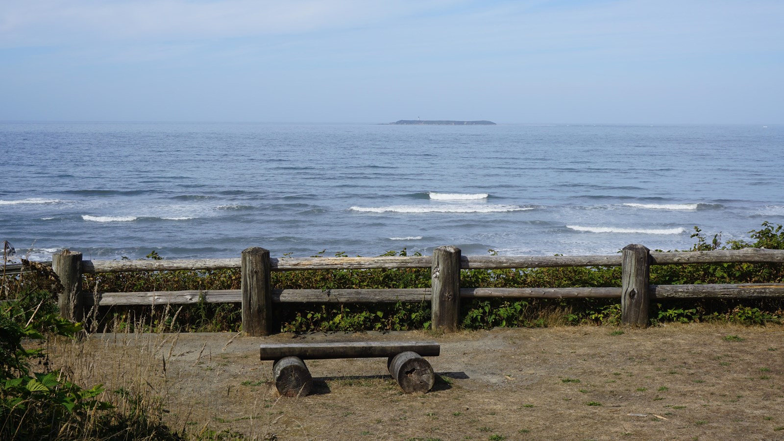 A wooden bench and a fence overlook the ocean.