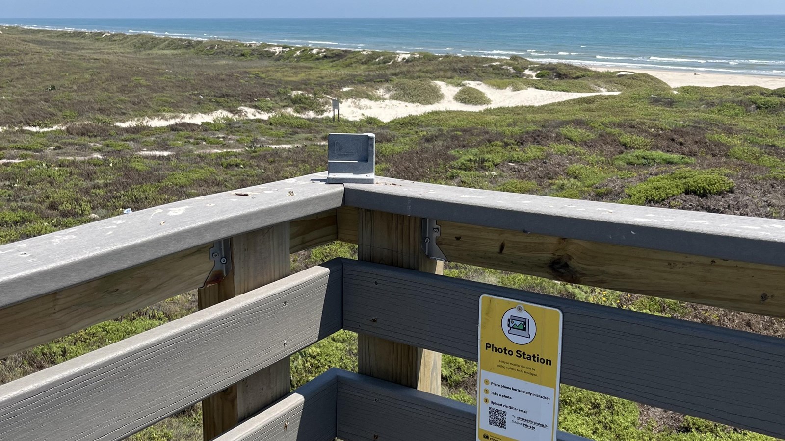 A photo monitoring station attached to a wooden railing with the Gulf in the distance. 