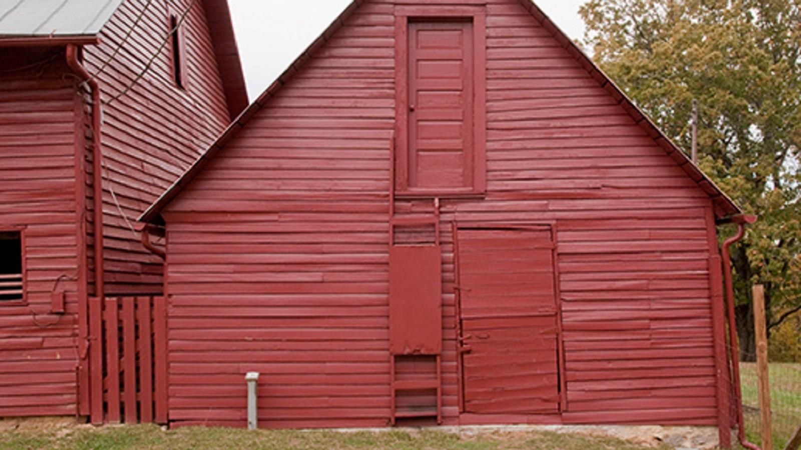 Red barn structure with 2 doors and a ladder on the front to access top door.