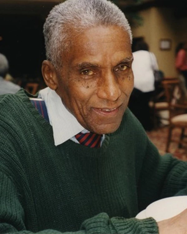 An older black man with short white hair seated at a table.