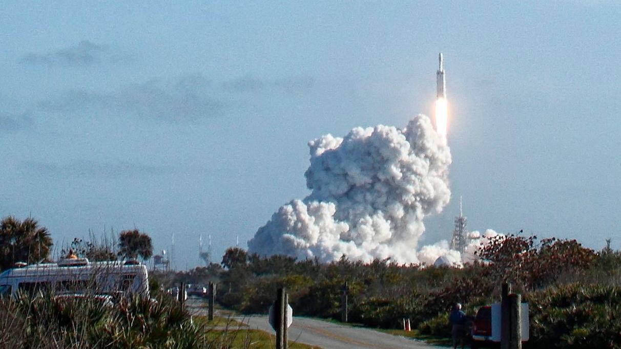 Falcon heavy launch with trees and roadway in foreground,