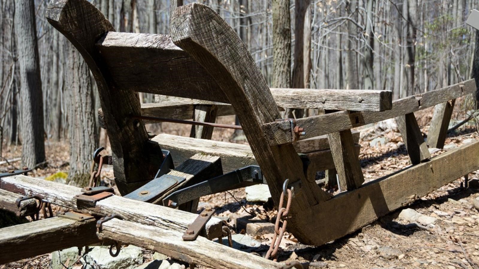 A large wooden sled resting on top of rocks alongside a trail in the forest.