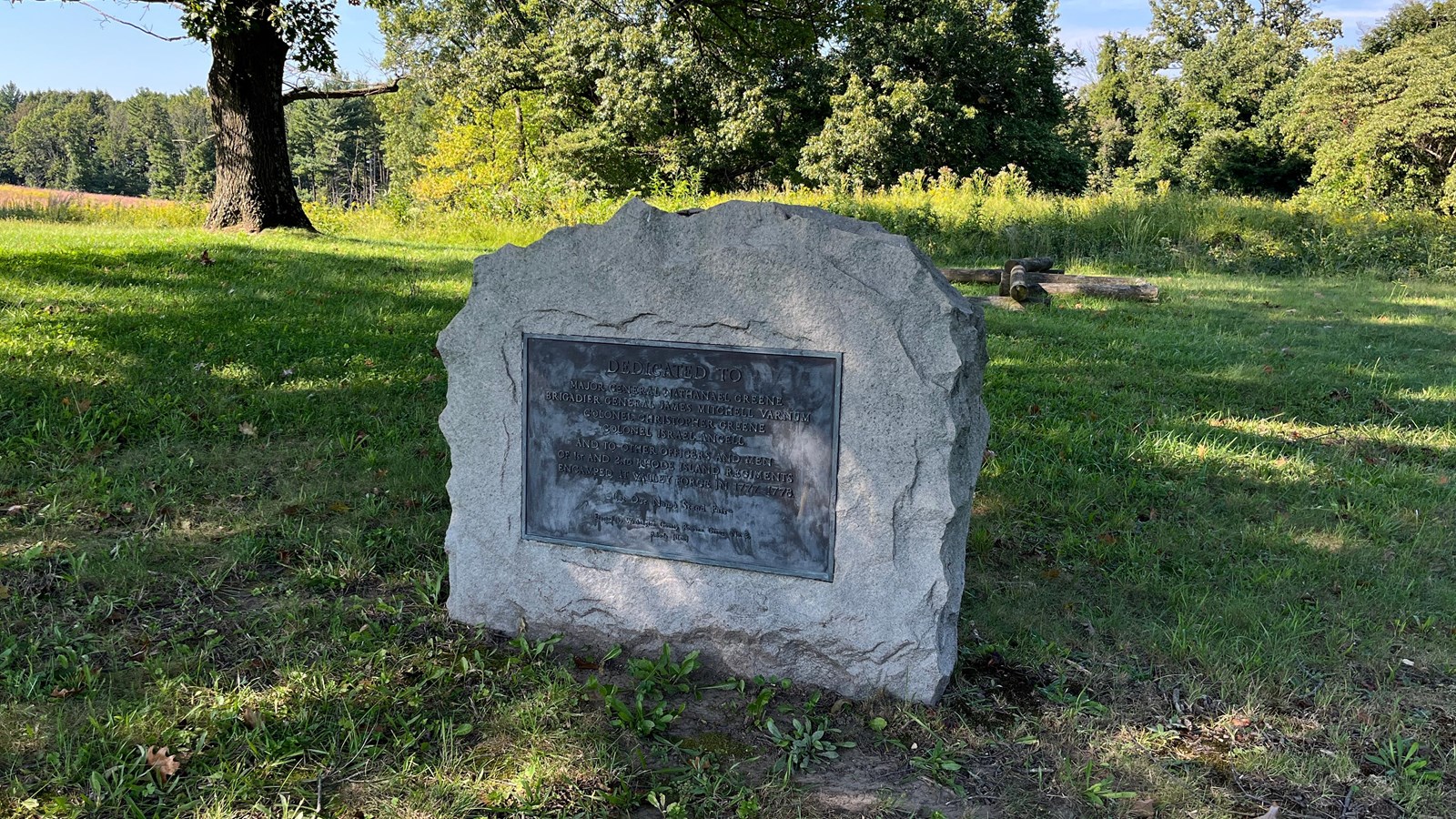 A stone slab monument with a bronze plaque on a grassy lawn.