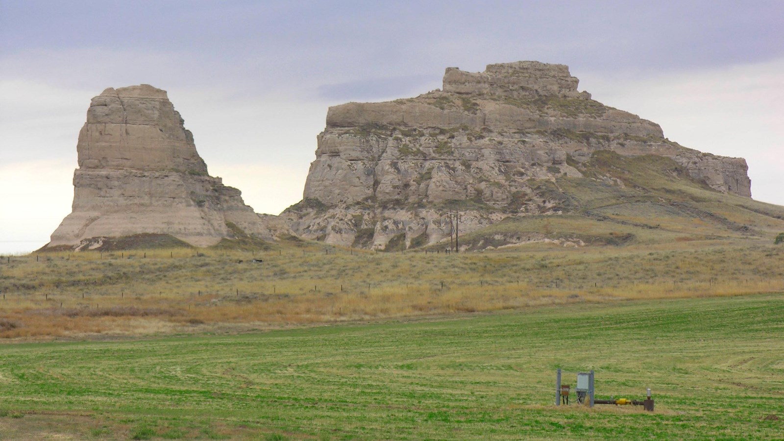 Two large stone monoliths stand in the distance of a mowed grass field.