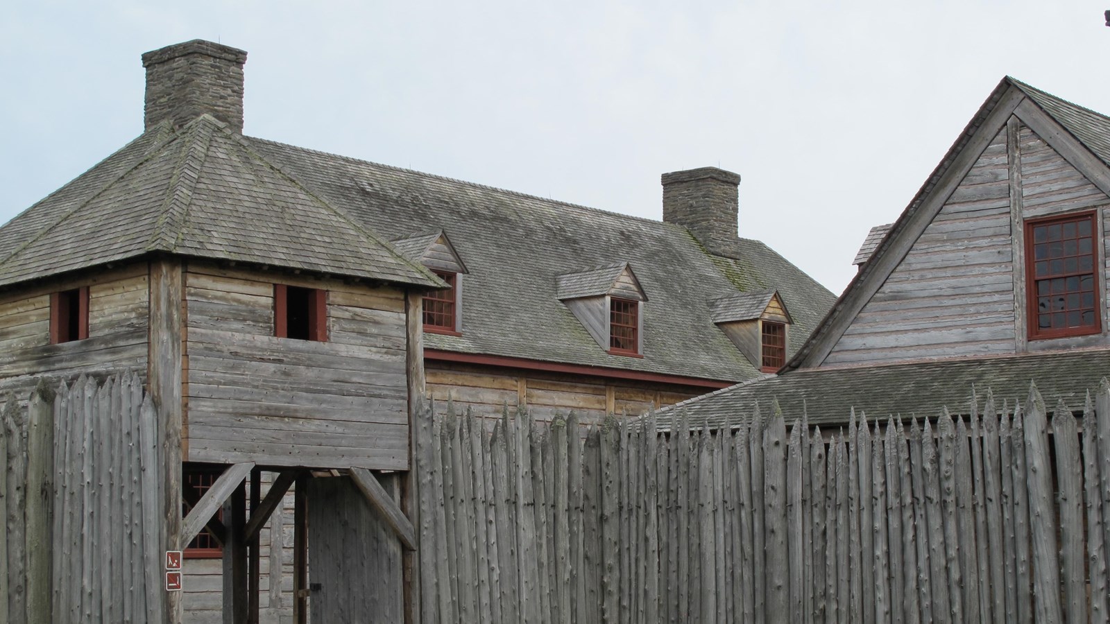 Wooden palisade in front of historically reconstructed unpainted wood buildings