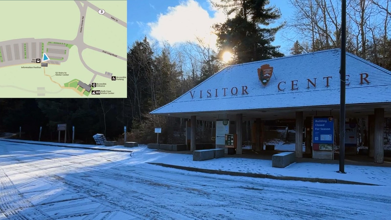 Winter photo of a roofed, outdoor parking lot pavilion with an NPS arrowhead and Visitor Center sign