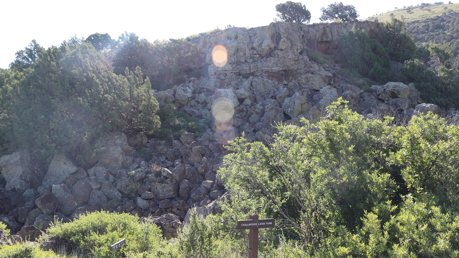 Jumble of grayish black volcanic rock and sign for a collapsed lava tube